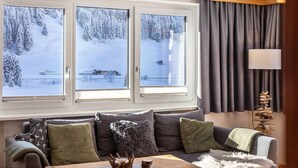 Ein gemütliches Wohnzimmer mit einer Couch, einem Holztisch und drei Fenstern mit Blick auf Schnee.