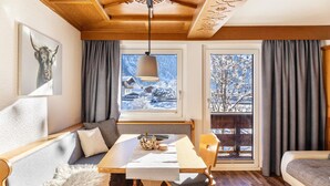 A cozy room with a wooden ceiling, a dining table, a sofa, and a view of a snowy landscape. - Apartment 'Hahnenkamm - 12' with Mountain View, Private Balcony and Wi-Fi (Nesselwängle)