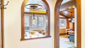 A hallway with arched doorways leading to a dining area with a table and chairs, a kitchen area with a sofa, and a view of a snowy landscape through a window. - Apartment 'Schneidspitze - 18' with Mountain View, Private Balcony and Wi-Fi (Nesselwängle)