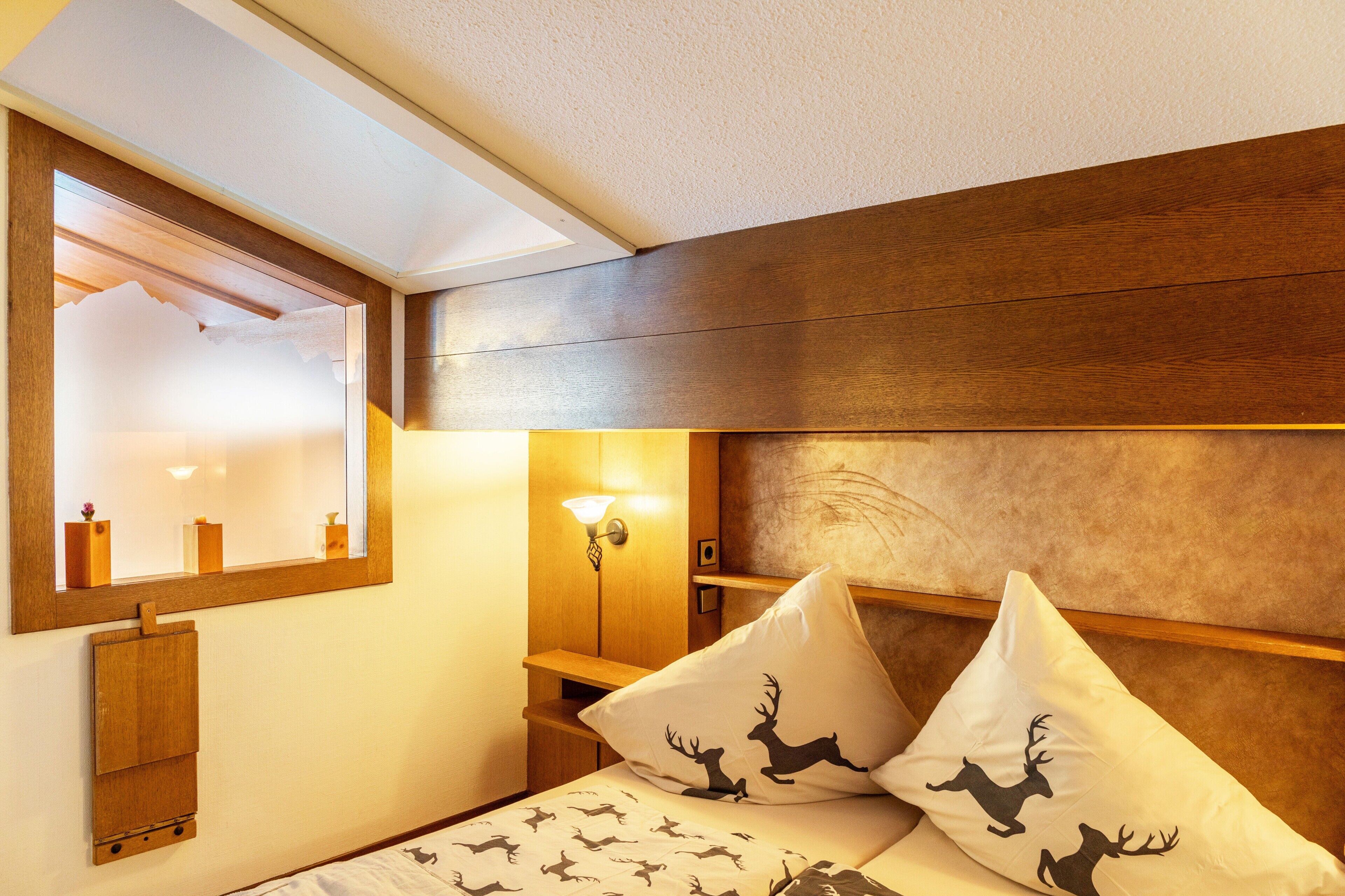 Ein Schlafzimmer mit einem Holzkopfteil, einem Spiegel, einem Nachttisch und zwei Kissen mit Hirschsilhouetten.