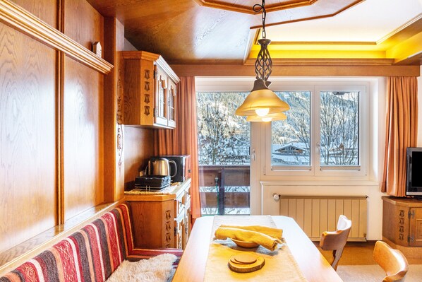 Habitación acogedora con un banco de madera, una mesa de comedor con una toalla amarilla, un televisor y vistas a árboles nevados a través de amplias ventanas.