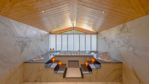 Een moderne badkamer met een houten plafond, marmeren wanden, een groot raam en een ingebouwd bad.