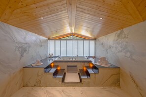 Un baño moderno con techo de madera, paredes de mármol, un ventanal grande y una bañera empotrada.