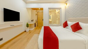 Een moderne hotelkamer met een groot bed, een flatscreen televisie aan de muur, een kleine potplant en een zichtbare badkamer door een open deur.