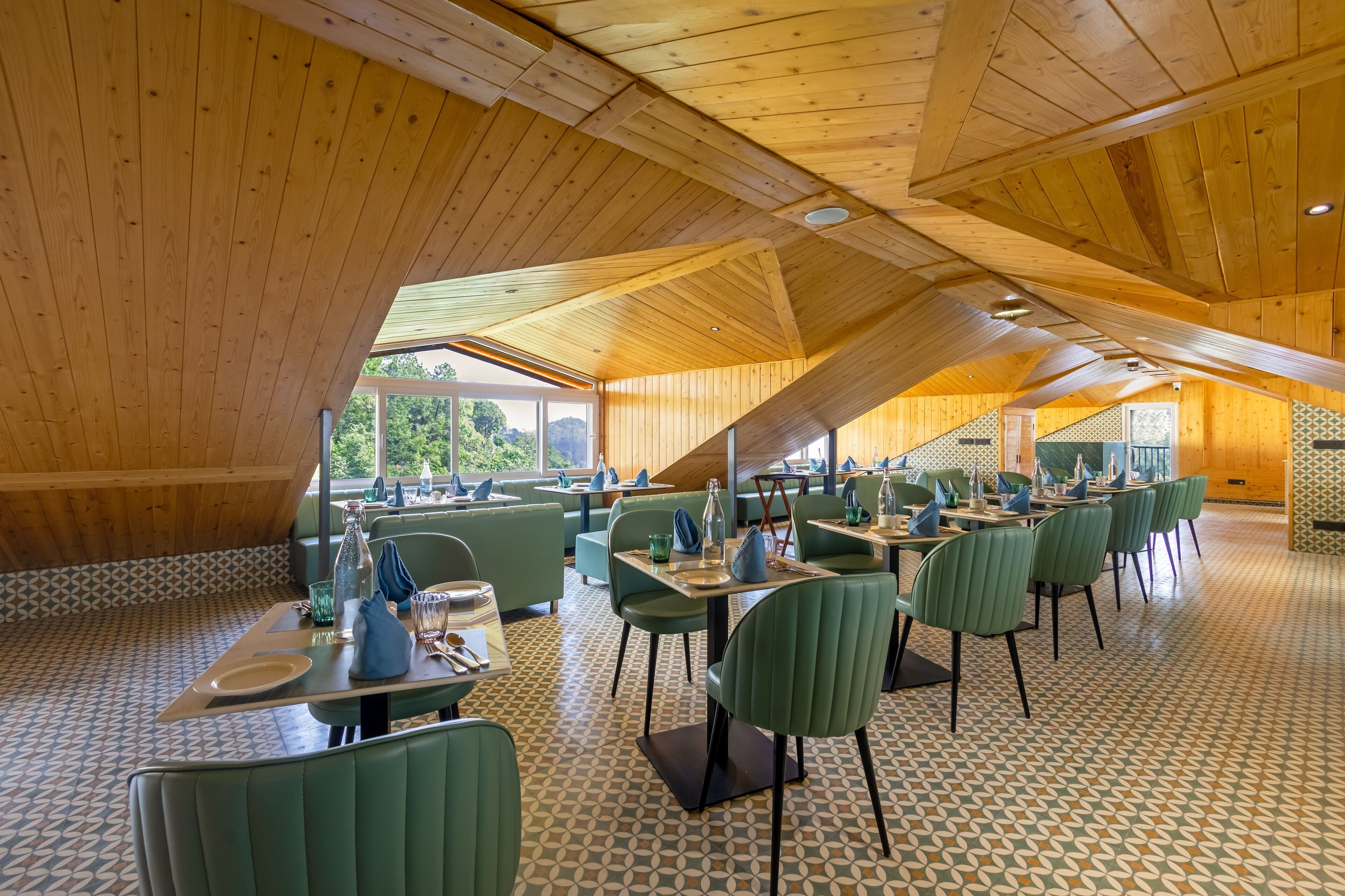 A spacious dining area with wooden ceiling beams, green upholstered chairs, and patterned floor tiles.