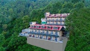 Een hotel met meerdere verdiepingen en balkons, gelegen tegen een achtergrond van dicht bos en heuvels.