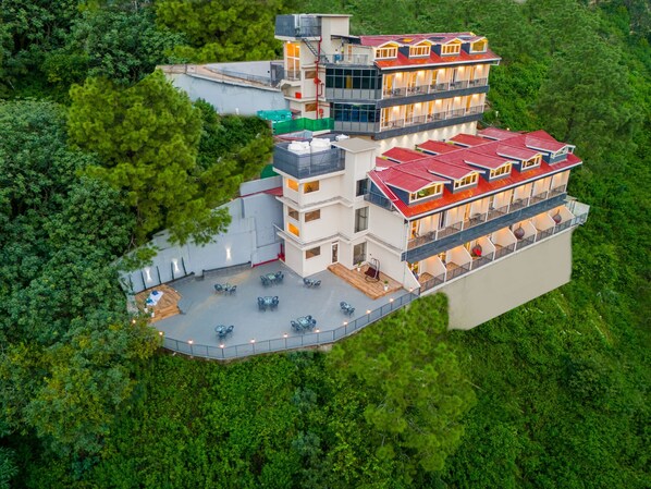 Un hotel de varios pisos con terraza en la azotea y múltiples balcones.