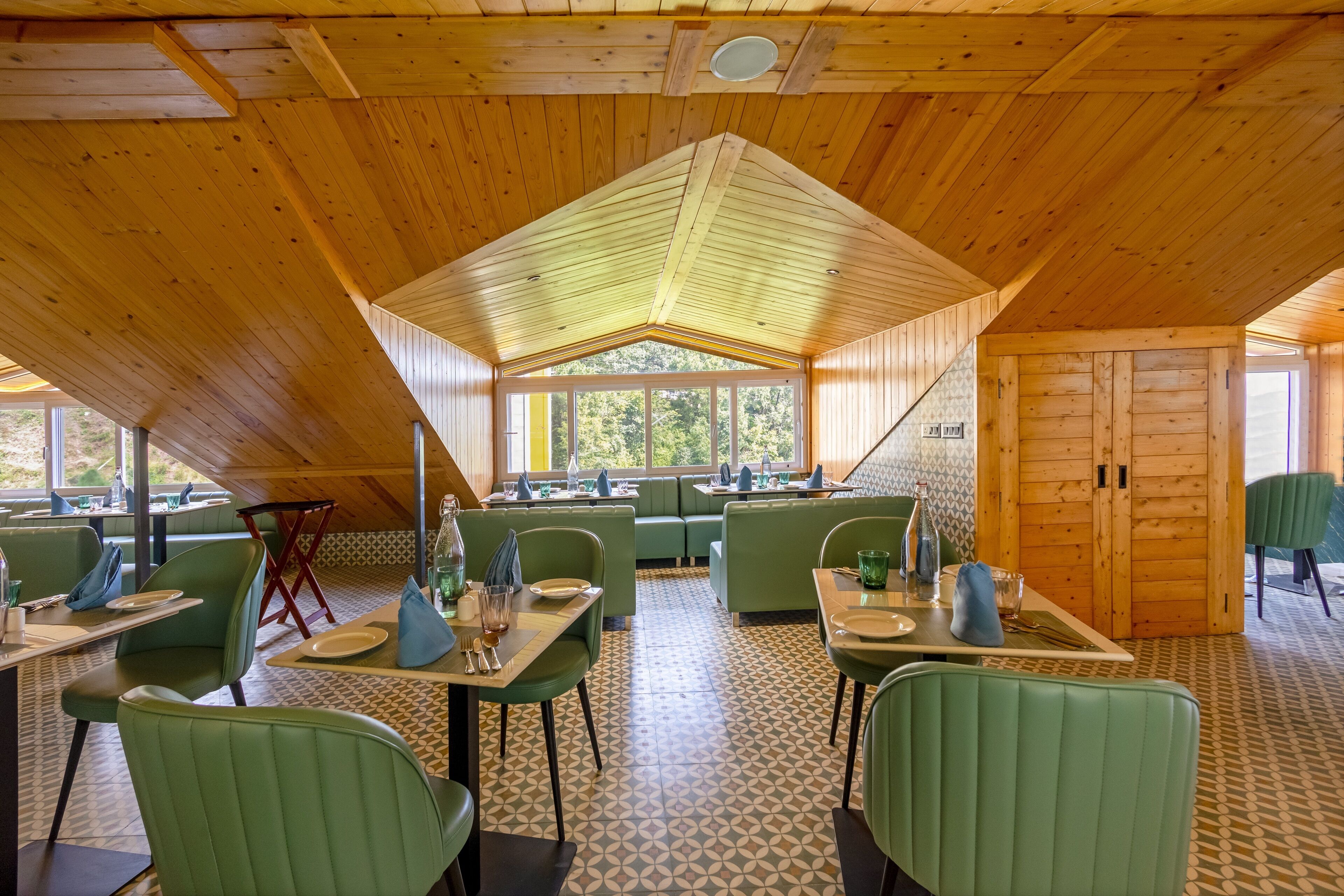 Un restaurante con asientos y mesas verdes, techo de madera y suelo de baldosas estampadas.