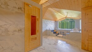Een houten sauna met een marmeren vloer, een houten deur en een raam met uitzicht op groen.