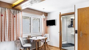 Una stanza con un letto, un tavolo con sedie, una TV e un bagno visibile attraverso una porta aperta.