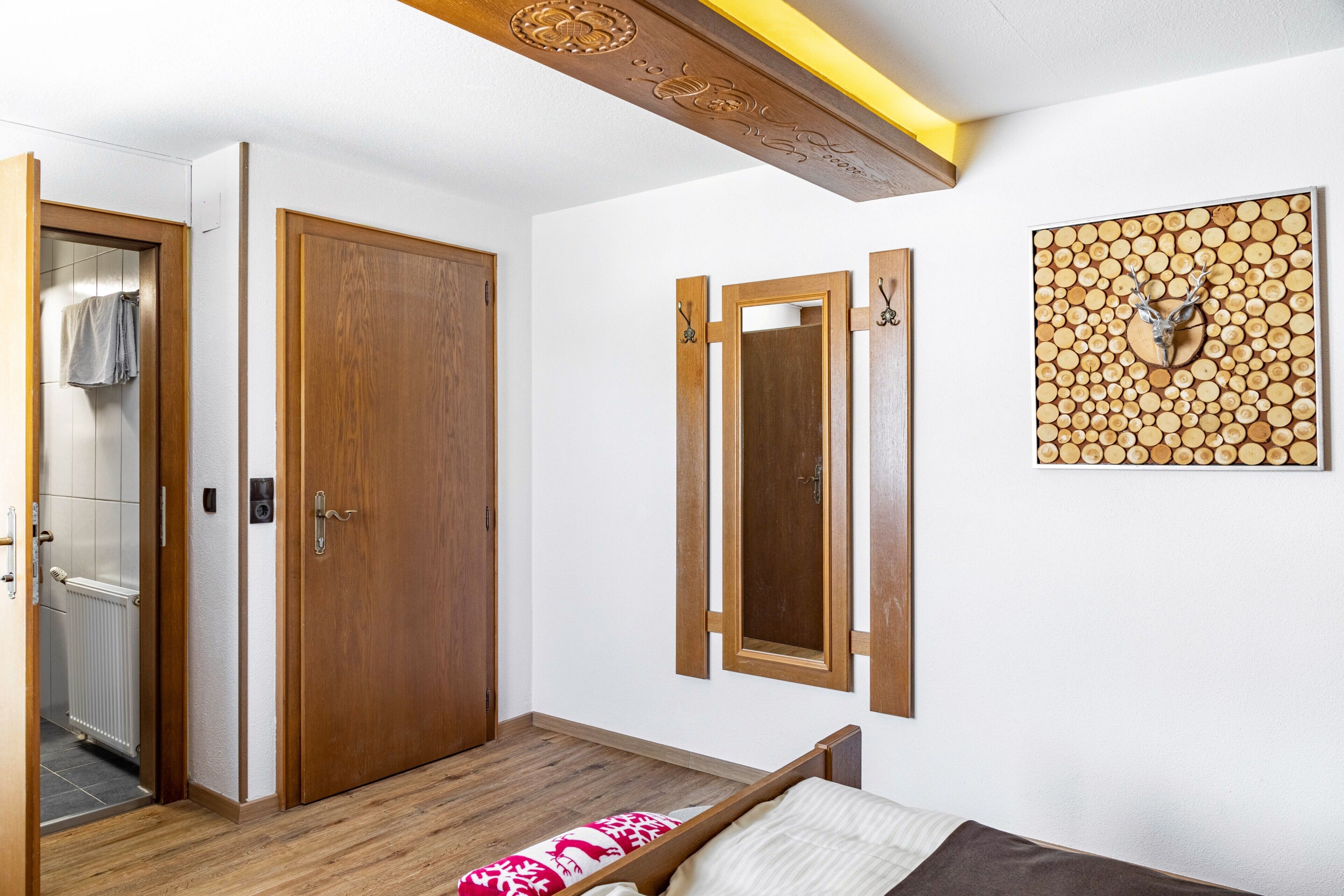 Une chambre avec une porte en bois, un miroir, un lit recouvert d’une couverture à motifs et une œuvre d’art accrochée au mur.