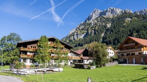 Un borgo montano con edifici in legno tradizionali, cielo sereno e una montagna imponente sullo sfondo.