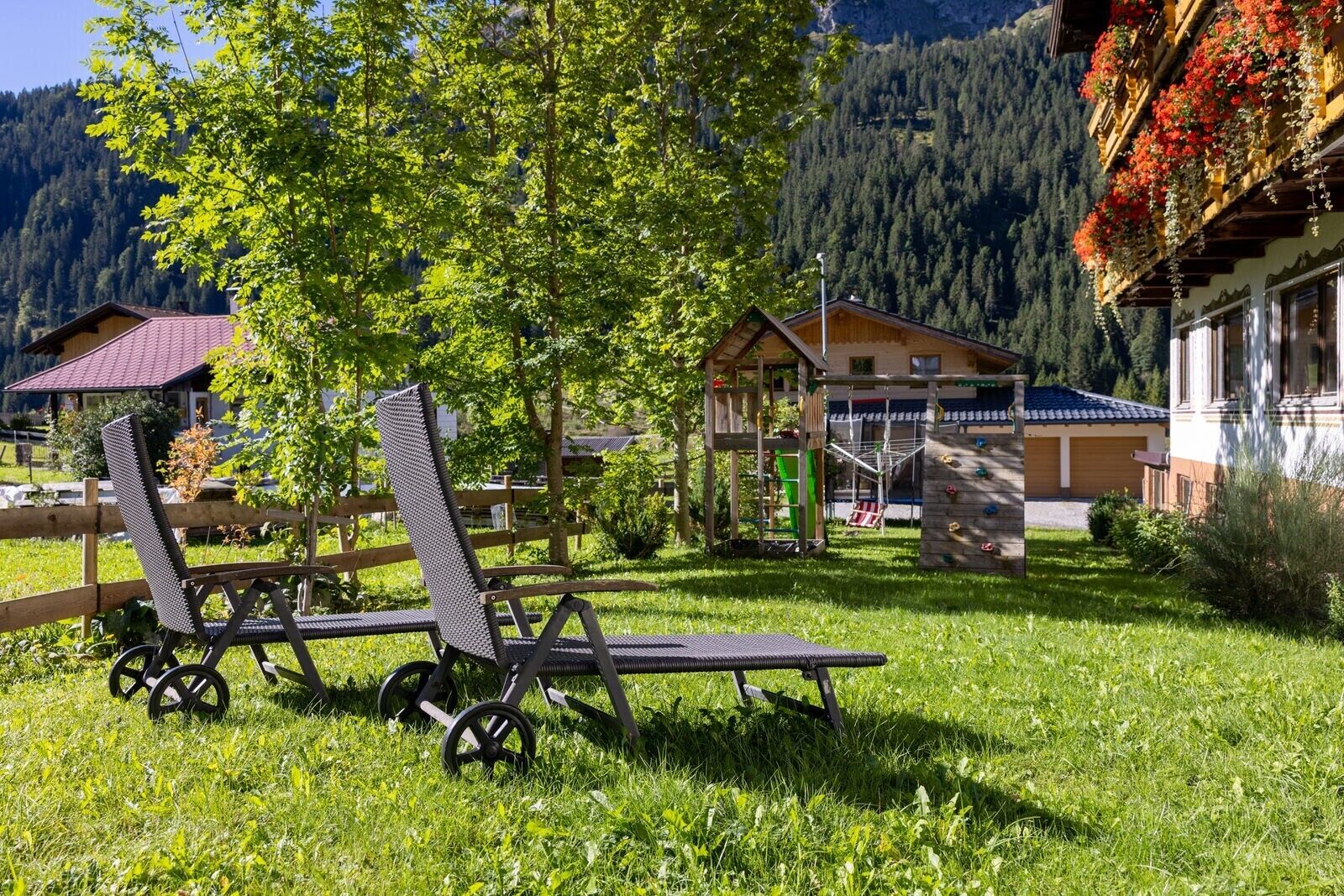 Une terrasse en bois avec une chaise et une table, un mur d’escalade et un bâtiment avec un toit rouge, le tout situé dans une région montagneuse.