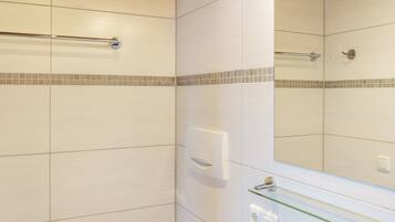 A bathroom with white tiles, a glass shower enclosure, and a mirror reflecting the room.