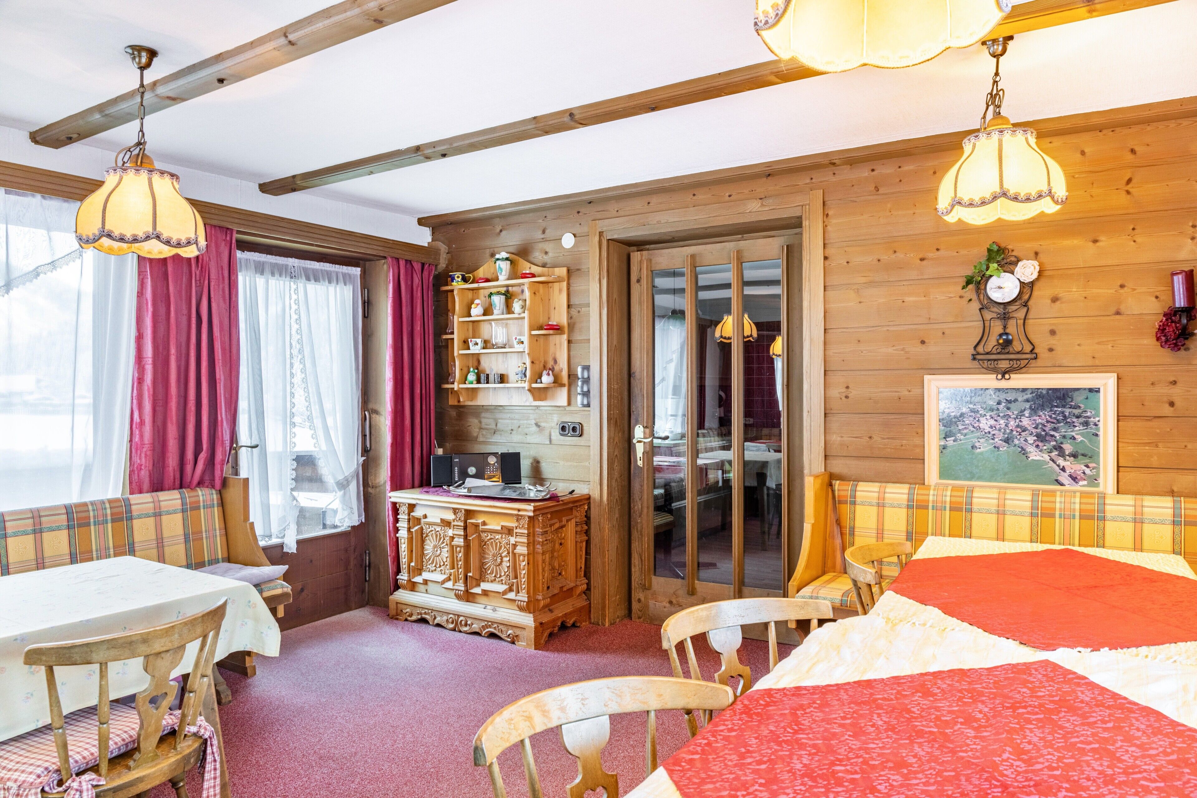 A cozy room with a wooden ceiling, a dining table, a sofa, a wooden cabinet, and a bed with a red blanket.