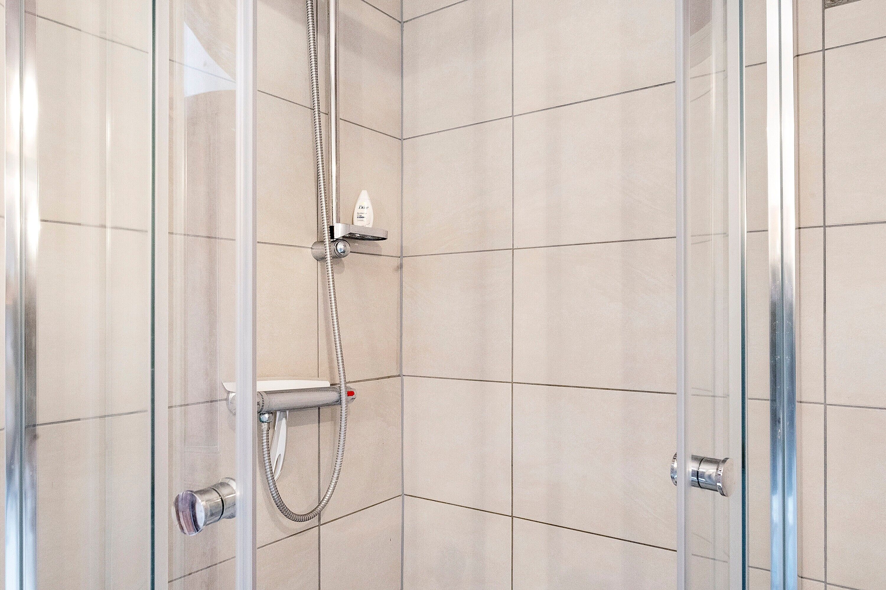 Een douchecabine van glas met een handdouche en een bedieningspaneel aan de muur.