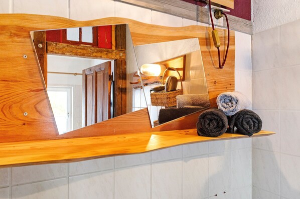 Un comptoir en bois avec un miroir qui reflète une pièce, une lampe et des serviettes enroulées.