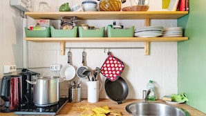 A kitchen with a stove, pots, a sink, and shelves with dishes and kitchen utensils.