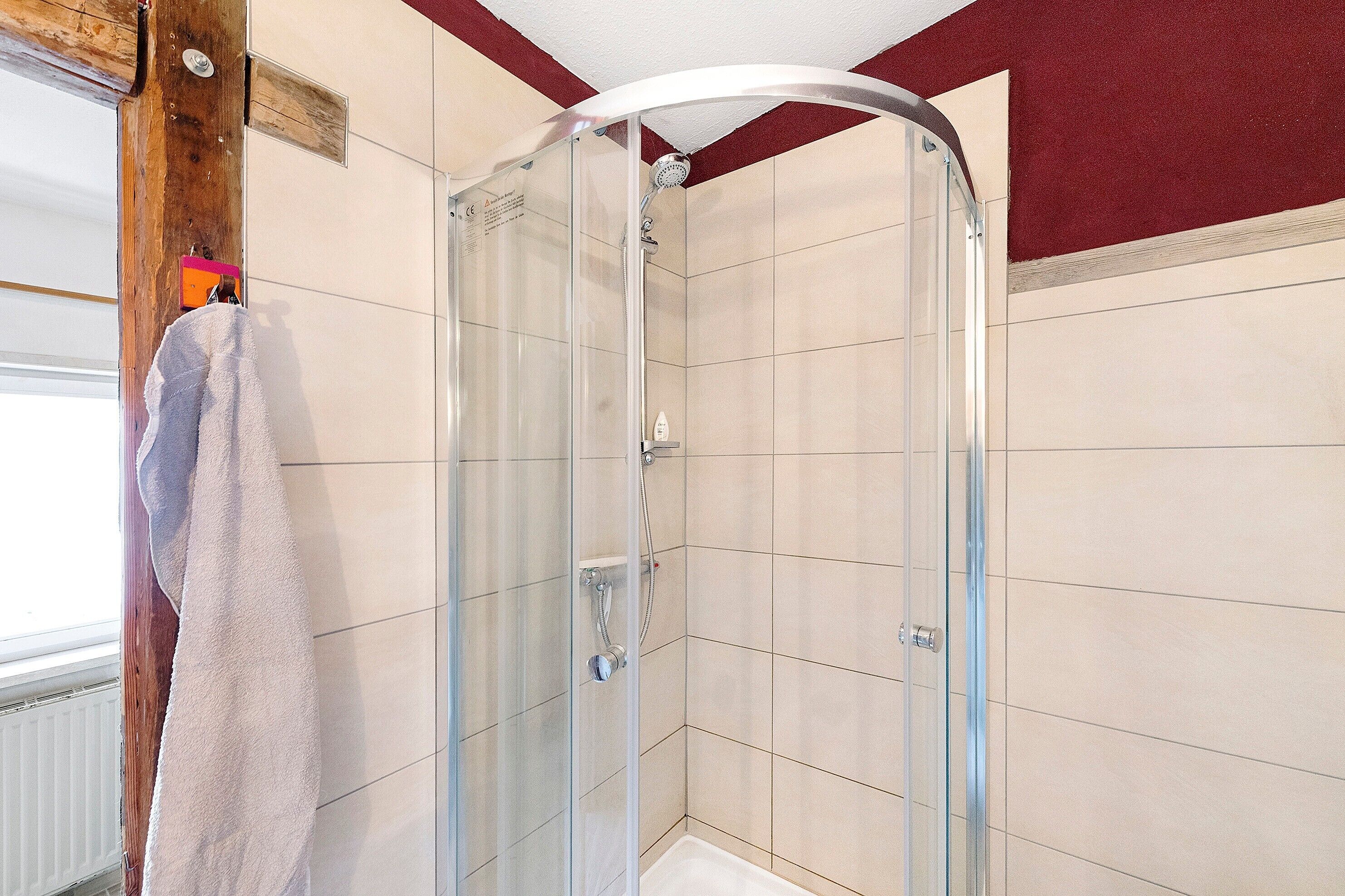 Eine gläserne Dusche mit weiß gefliesten Wänden, ein Handtuch an der Tür und eine Holzträgerkonstruktion.