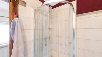 Eine gläserne Dusche mit weiß gefliesten Wänden, ein Handtuch an der Tür und eine Holzträgerkonstruktion.