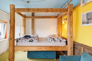 A room with a wooden bunk bed, a window with curtains, a bedside table, and a lamp.