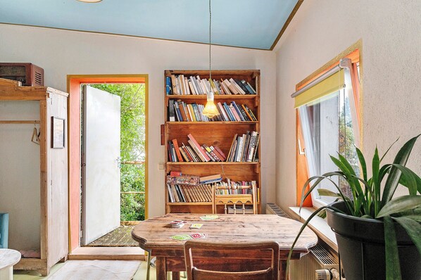 A cozy reading nook with a wooden bookshelf, a table, and chairs, and a potted plant.