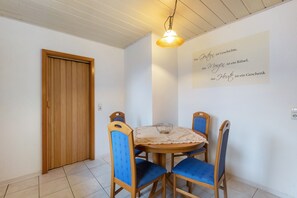 Ein Essbereich mit einem Holztisch, blau gepolsterten Stühlen, einer Hängeleuchte und einer Wand mit deutschem Text.