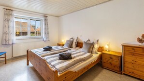 Une chambre à coucher avec un lit en bois, une table de chevet, une commode, une fenêtre avec des rideaux et un radiateur.
