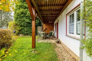 Un portico coperto con tavolo e sedie, un pergolato in legno e un edificio bianco con una finestra.
