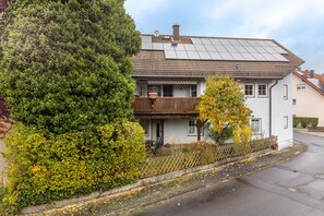 Ein zweistöckiges Haus mit Balkon, Solaranlage auf dem Dach und einem Zaun.