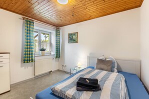Una camera da letto con un letto, un comodino, una lampada, una finestra con tende, un termosifone e un quadro appeso al muro.