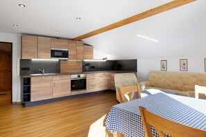 A modern kitchen with wooden cabinets, a built-in oven, and a dining area with a checkered tablecloth.