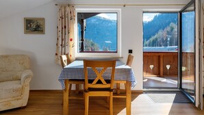 A room with a wooden dining table, a wooden chair, a sofa, and a window with a mountain view.