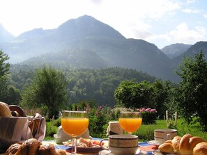 A breakfast table with food and drinks, set against a mountainous backdrop.