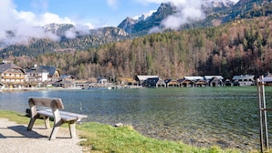 En vy över en sjö med en bänk, byggnader och berg i bakgrunden.