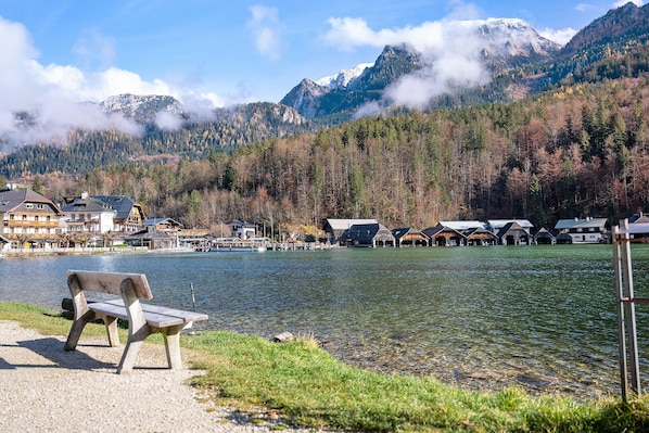 A lakeside view with a bench, buildings, and mountains in the background.