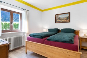 Ein Schlafzimmer mit einem hölzernen Bett, einem Fenster mit Aussicht, einem Heizkörper und einem Bild an der Wand.