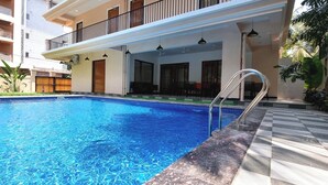 A swimming pool with a checkered border, surrounded by a building with balconies and outdoor seating. - CALANGUTE BEACH VILLA By SEVEN HOTELS (Calangute)