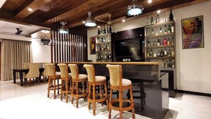 A bar area with wooden bar stools, a television, and a shelf with various bottles. - CALANGUTE BEACH VILLA By SEVEN HOTELS (Calangute)