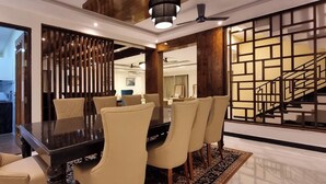A dining area with a dark wooden table and beige upholstered chairs. - CALANGUTE BEACH VILLA By SEVEN HOTELS (Calangute)