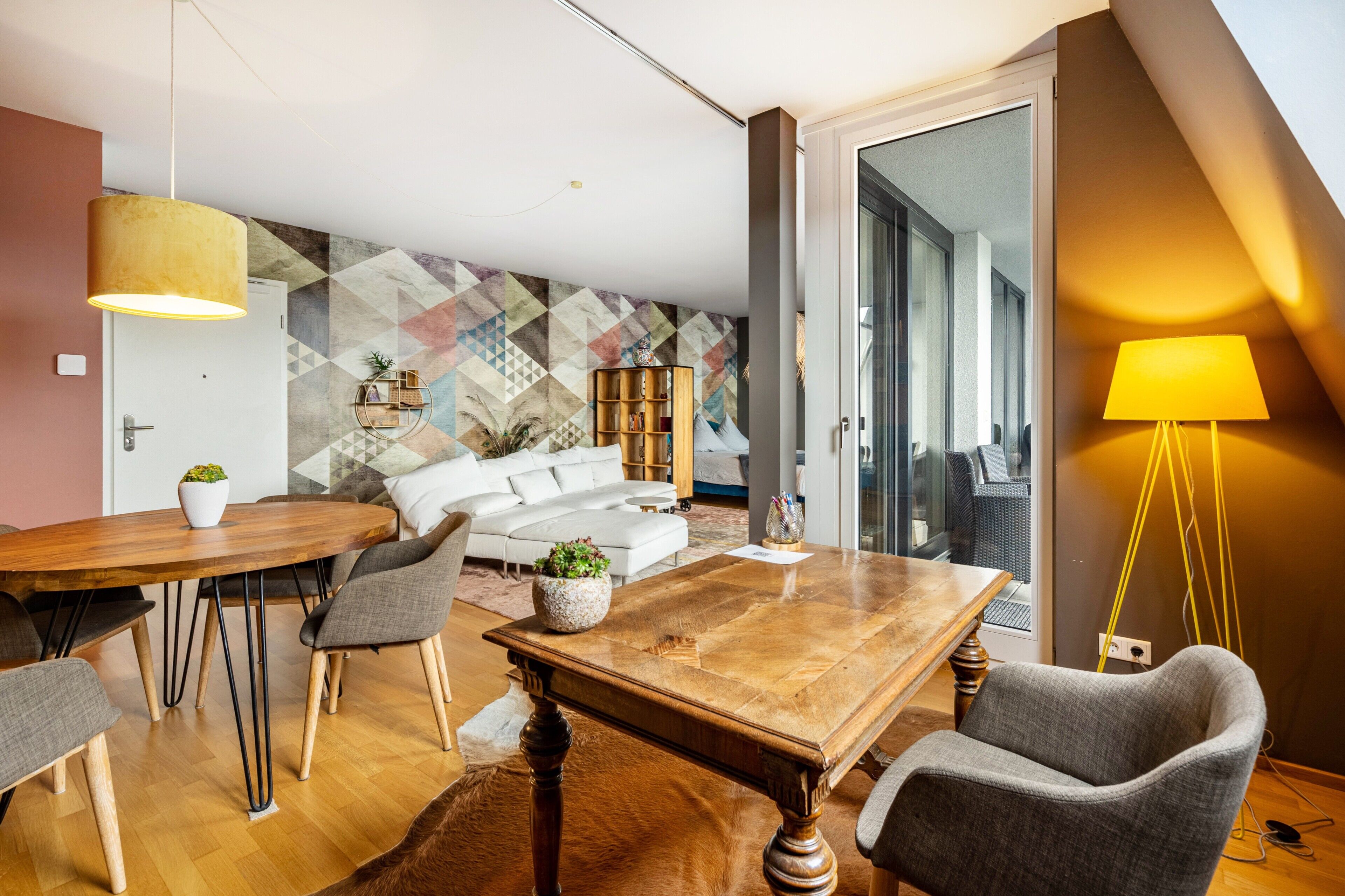 Ein modernes Wohnzimmer mit einem Holzessttisch, grauen Stühlen, einem weißen Sofa und einer strukturierten Wand.