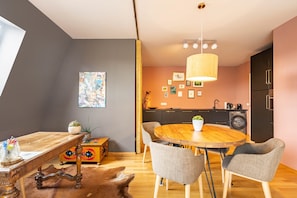 Un comedor con una mesa y sillas de madera, una lámpara colgante y una cocina al fondo.