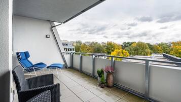 A balcony with outdoor seating, potted plants, and a view of trees and buildings.
