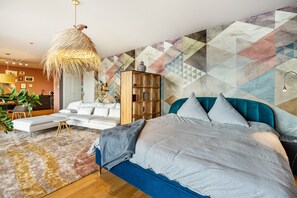 Un dormitorio moderno con una cama grande, un sofá, un armario de madera y una pared con estampado geométrico.