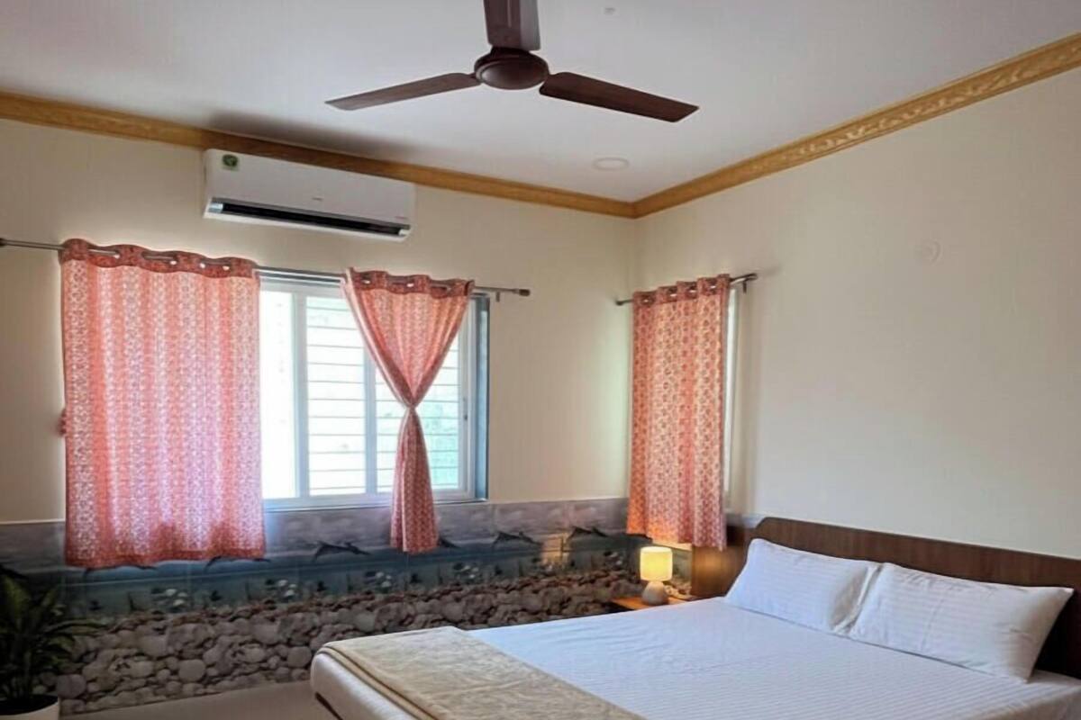 Un dormitorio con cama, ventilador de techo, aire acondicionado y ventana con cortinas.