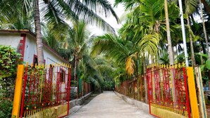 A pathway flanked by red and yellow gates leading to a building with a white exterior and red trim. - Saaj Villa (Nagaon)