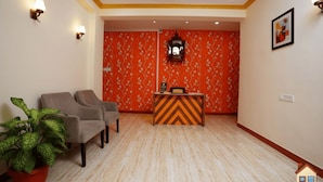 A reception area with a check-in counter, two armchairs, a potted plant, and a patterned wall. - Saaj Villa (Nagaon)
