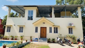 A two-story building with a central entrance, a swimming pool, and several potted plants. - Saaj Villa (Nagaon)
