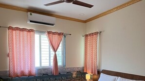 A bedroom with a bed, a ceiling fan, a window with curtains, and a stone wall. - Saaj Villa (Nagaon)
