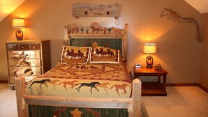A bedroom with a bed featuring horse-themed bedding, a wooden headboard with animal carvings, and two bedside lamps.
